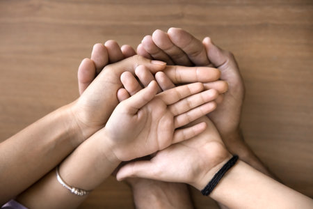 Caring mother, father and their two little kids stacked their palms together, as symbol of...