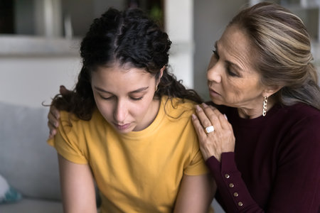 Close up of sad teenage girl and mature mother sit together on sofa, parent ask forgiveness after...
