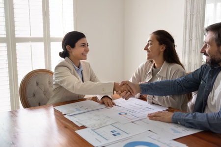 Positive Indian financial expert shaking hands with Caucasian husband and wife after analyzing personal finance for investment, saving, giving consultation, finishing consultation with handshakeの写真素材