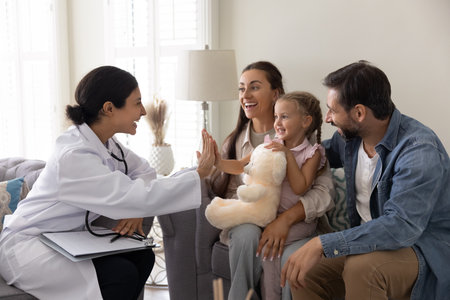 Happy doctor visiting little patient girl and her parents at home, giving high five hand gesture to positive healthy kid after successful therapy, examination, checkup, smiling, laughingの写真素材