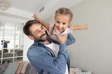 Cheerful father enjoying playtime with playful little girl, playing airplane flight, holding kid with open hands over shoulder, cuddling beloved cute daughter child, laughing, having funの写真素材