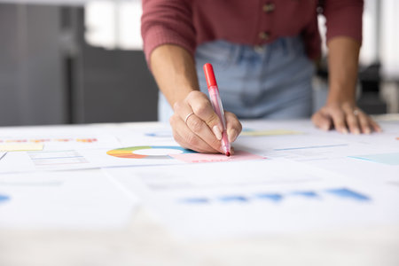 Cropped shot of female project manager writing notes on paper reports, using felt pen, analyzing statistic marketing data, working on financial business plan for startup. Hand close upの写真素材