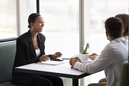 African professional woman leads negotiations with couple seated at table in office. Advisor or consultant explain contract details, share information about services, enjoy friendly talk with clientsの写真素材