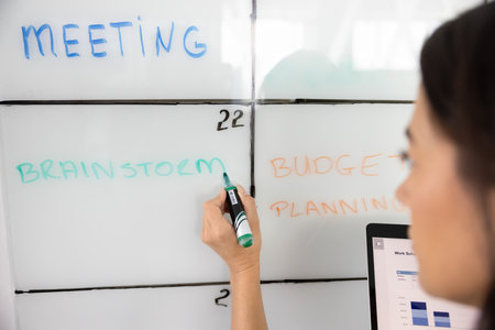 Female project manager planning work on project, teamwork, writing tasks on whiteboard in table cells, making Kanban scrum board for effective productive management. Cropped shot of businesswomanの写真素材