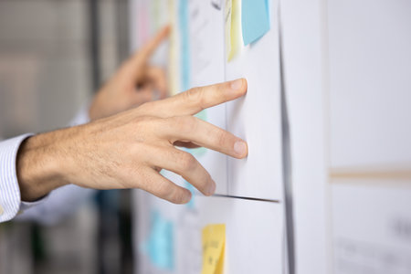 Hand of business project manager man pointing at whiteboard with colorful stickers, using agile...