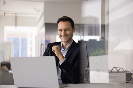 Happy business executive man working at computer at office workplace, typing, laughing, using job application, software, web service for online communication. Candid shot with copy spaceの写真素材
