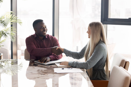 Multiracial business partners shaking hands at conference desk in office, as positive outcome of job...