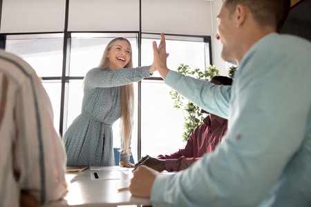 Cheerful European businesswoman gives high-five to male colleague in modern boardroom. Gesture of...