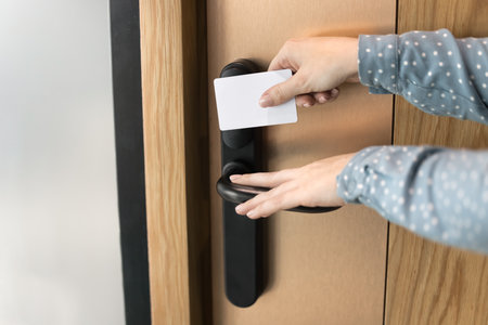 Close up of unknown female hands touching handle, hold white pass card, opening hotel or office room door. Unrecognizable woman using keycard to access modern door with lock. Security, safety, entryの写真素材