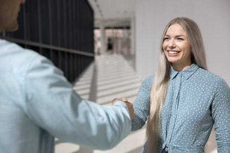 Attractive European female applicant and HR manager shaking hands, getting acquainted, met in corporate office hallway before job interview. Good first impression, business etiquette, gender equalityの写真素材