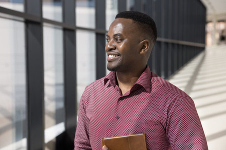 Pensive African businessman, staff member dressed in casual shirt standing alone in modern office...