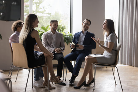 Group of smiling, positive company employees solve business engaged in teambuilding with woman boss or business coach, businesspeople looking happy, enjoy pleasant talk, friendly atmosphere at meetingの写真素材