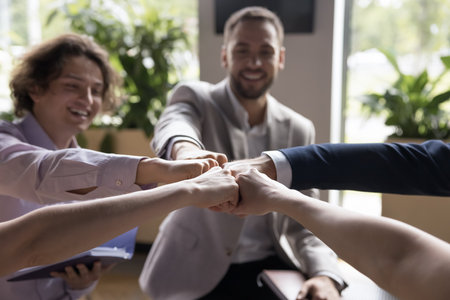 Close up happy teammates sit in circle join fists together, share common success, showing unity,...