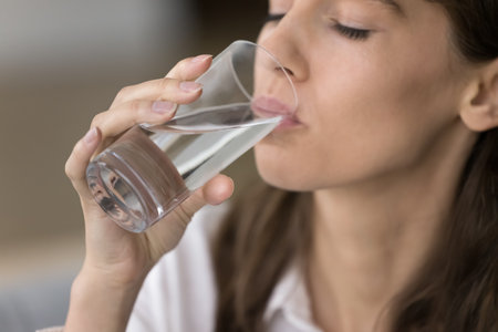 Glass of natural fresh water in female hand close up. Young beautiful woman drinking clean pure...