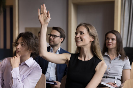 Smiling woman employee, educational seminar participant raise arm to ask question engaged in...