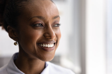 Face close up of happy thoughtful young African American woman, smiling, showing teeth, thinking, looking at copy space away.の写真素材
