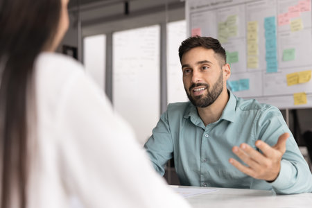 Positive young Latin business professional man talking to employer on job interview. Businessman speaking to partner at meeting table, discussing collaboration, partnershipの写真素材