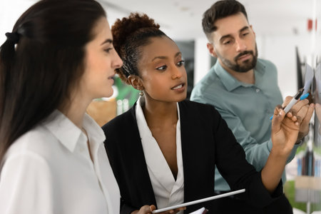 Focused inspired business leader woman presenting project plan on Kanban board to team, making tasking, scrum management scheduling on whiteboard, writing, telling ideasの写真素材
