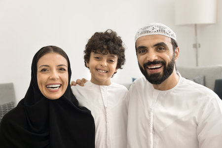 Head shot portrait of happy Muslim couple with son. Cute little boy posing for camera with loving mother and joyful father, dressed in traditional Arabian abaya and dishdasha dress. Culture, familyの写真素材