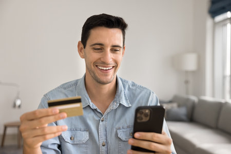 Hispanic man holds credit card and cellphone, purchasing via marketplace application, make easy, continent remote payments, paying bills, spending money, getting cashback, feel satisfied.の写真素材