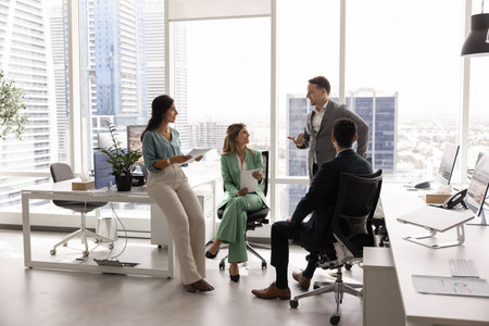 Small business team discussing teamwork in city office space, standing and sitting in circle, talking in workspace, planning work strategy, tasks, brainstorming on ideas for projectの写真素材