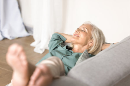 Peaceful relaxation. Sleepy carefree elderly lady retiree relax nap dream on comfy couch hands behind head enjoy breathing fresh conditioned air listen to music relieving stress in moment of serenityの写真素材