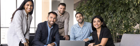 Team of diverse corporate staff members gathered in modern office, exuding professionalism, achievements and unity, wide view. Five young and mature employees posing for camera with joyful expressionの写真素材