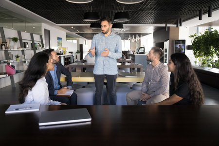 Young Hispanic man team leader, boss or staff member represent idea and work-related matter solution to employees colleagues at meeting in modern coworking office. Briefing event, brainstorm sessionの写真素材