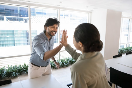 Two happy Indian teammates exchanging high-five, succeed joint goal, accomplish project successfully, get positive outcome and sales growth, making gesture of unity, synergy and respect. Partnershipの写真素材
