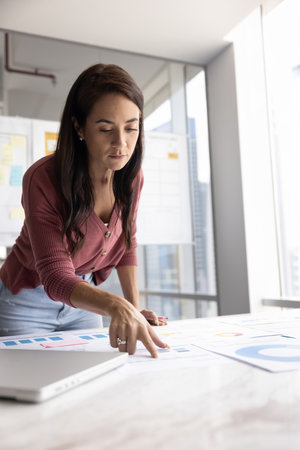 Business analyst at work. Young woman executive entrepreneur develop startup make finance forecast engaged in market strategy planning based on paper statistic reports at corporate office. Copy spaceの写真素材
