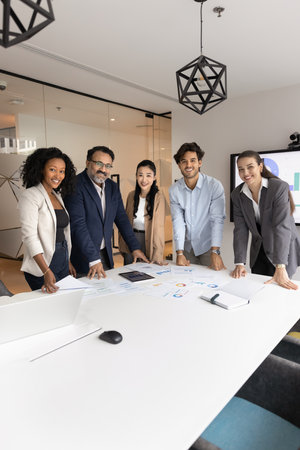 Group of diverse businessmen and businesswomen standing around conference desk in modern office,...