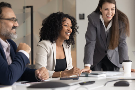 Laughing multiethnic teammates, corporate staff members having positive communication gathered at conference table during briefing or teambuilding, looking satisfied with teamwork or meeting outcomeの写真素材