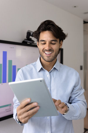 Smiling professional businessman working on digital tablet in office, editing files or documents,...