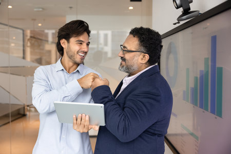 Young 30s and mature 45s multiethnic teammates standing in modern office, sharing fist bump, gesture of camaraderie, mutual respect, and celebration of joint success. Strong collaboration and teamworkの写真素材