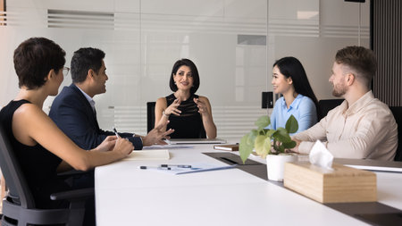 Attractive businesswoman and teammates collaborate on presentation, analyze status of ongoing project, discussing next steps, provide feedback and planning improvements, gathered at conference tableの写真素材