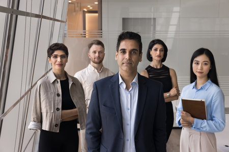 Human resources. Group of serious employees standing together in office, posing for camera led by mature serious professional Indian team leader or boss, showing professionalism, reliability and unityの写真素材