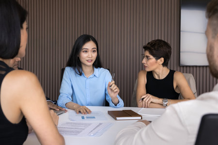 Asian businesswoman leads formal meeting with diverse corporate team, reviewing data, discussing...