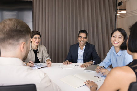 Happy diverse teammates take part in workshop or training session gathered at conference table, laughing, enjoy friendly interaction during corporate briefing in modern office. Teamwork, teambuildingの写真素材