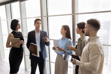 Team listening boss standing in office against panoramic window, leader provide explanations,...