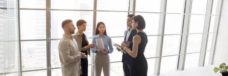 Group of five processionals discussing work-related matters gathered in modern office standing...