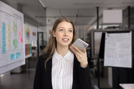 Positive ambitious young 20s businesswoman in formal suit recording voice message, speaking on...