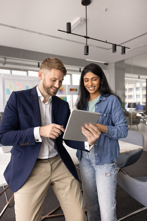 Happy young Caucasian businessman showing online content on digital tablet to female Indian...