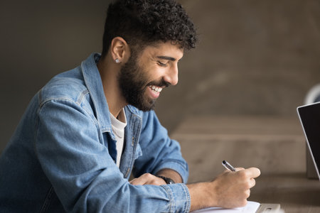 Busy and stylish. Smiling casual student hipster guy study alone write essay plan schedule take...