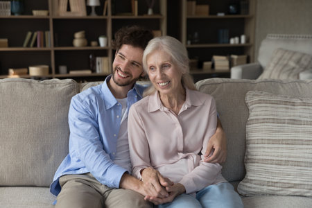 Peaceful moment with mommy. Smiling affectionate young man sit on couch hold elderly mother grandma...
