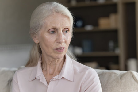Sadness of aging. Head shot portrait unhappy older woman sit on couch lost in unpleasant thoughts...