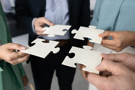 Close up of four businesspeople, corporate team holding large, blank puzzles in hands, extending and connecting pieces, as symbol of finding solution, engaged in effective teamwork and problem-solvingの写真素材
