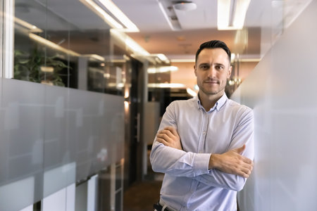 Confident handsome young Latin business owner man posing in stylish office corridor for successful...