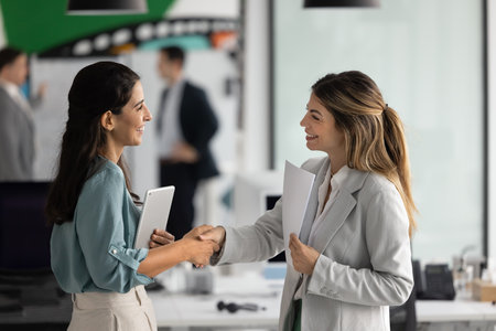 Two professional businesswomen shaking hands, greeting each other standing in modern office, making deal, concluding successful agreement or partnership, welcoming client, start business communicationの写真素材