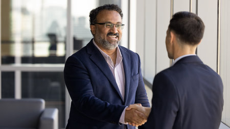 Cheerful older Indian business owner man shaking hands with younger Caucasian consultant, job...