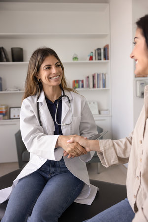 Happy young Latin doctor woman giving handshake to positive female patient, wishing getting better...